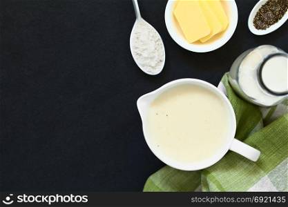 Homemade French Bechamel or White Sauce served in sauce boat with ingredients on the side (flour, butter, milk, pepper), photographed overhead on slate with natural light (Selective Focus, Focus on the sauce). Bechamel or White Sauce