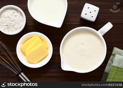 Homemade French Bechamel or White Sauce served in sauce boat with ingredients on the side (flour, butter, milk), photographed overhead on dark wood with natural light (Selective Focus, Focus on the sauce). Bechamel or White Sauce