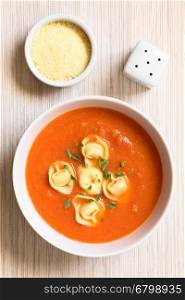 Homemade fresh cream of tomato soup with tortellini garnished with fresh oregano leaves, photographed overhead with natural light