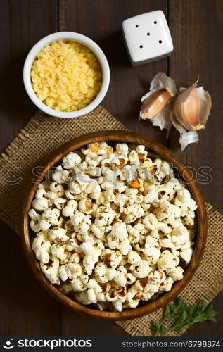 Homemade fresh savory popcorn with cheese, garlic and dried oregano in wooden bowl, photographed overhead on dark wood with natural light (Selective Focus, Focus on the top of the popcorn)