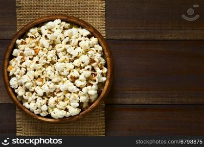 Homemade fresh savory popcorn with cheese, garlic and dried oregano in wooden bowl, photographed overhead on dark wood with natural light (Selective Focus, Focus on the top of the popcorn)