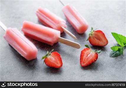 Homemade frozen strawberry ice cream popsicles and fresh strawberries on a concrete background. Summer dessert