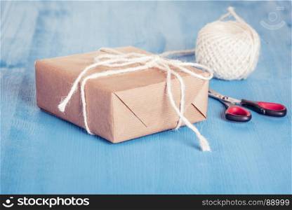 Homemade gift box wrapped with classic brown paper and tied with white string, scissors and twine in background