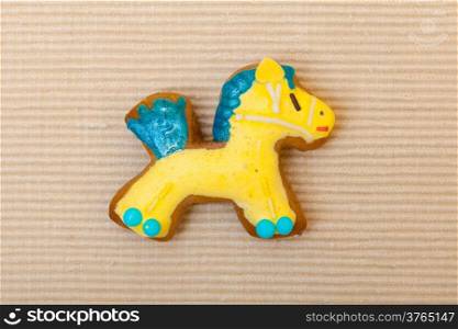 Homemade gingerbread cake pony with icing and blue yellow decoration on brown as christmas background. Holiday handmade concept.