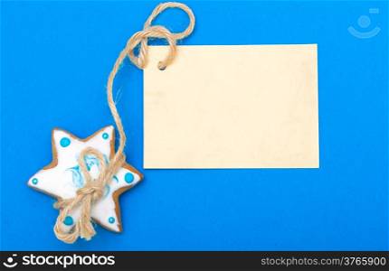 Homemade gingerbread cake star with icing and blue decoration and blank paper card copy-space on blue as christmas background. Holiday handmade concept.