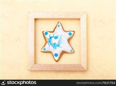 Homemade gingerbread cake star with icing and blue decoration in wooden frame on brown as christmas background. Holiday handmade concept.