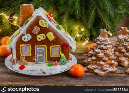 homemade gingerbread house with tangerines and christmas lights on wooden table. gingerbread house