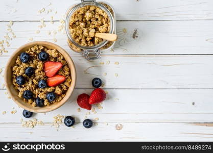 Homemade granola and fresh berries on wood table with space.