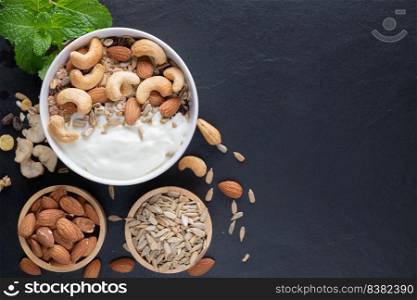 Homemade granola or muesli, bowl of oat granola with yogurt, almond, Cashew nuts, mint and nuts on the black rock board for healthy breakfast, copy space. Healthy breakfast menu concept.