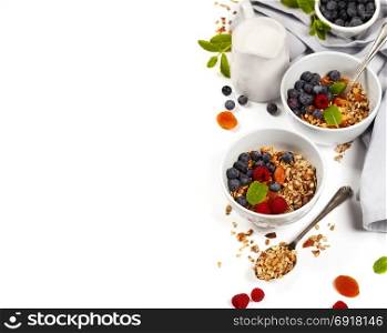 Homemade granola (with dried fruit and nuts) and healthy breakfast ingredients - honey, milk and berrieson white background