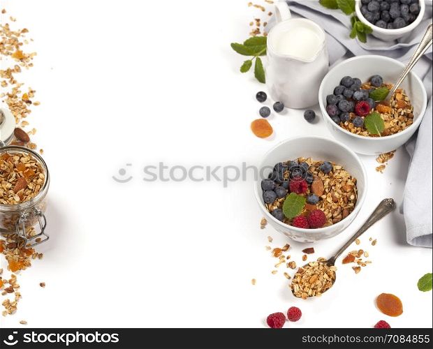Homemade granola (with dried fruit and nuts) and healthy breakfast ingredients - honey, milk and berries on white background