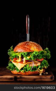 Homemade grilled burger with turkey cutlet, cheese, cheese sauce and vegetables on a wooden board, on a dark background. Close up, selective focus with copy space, vertical frame