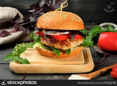 homemade hamburger with pork fried steak, red tomatoes, fresh round bun with sesame seeds on wooden board, close up