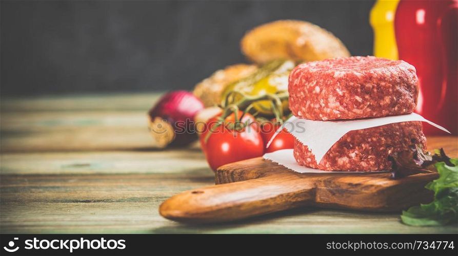 Homemade hamburgers. Raw beef patties and ciabatta bread with other ingredients for hamburgers on wooden background. Homemade hamburgers on wooden table, close up