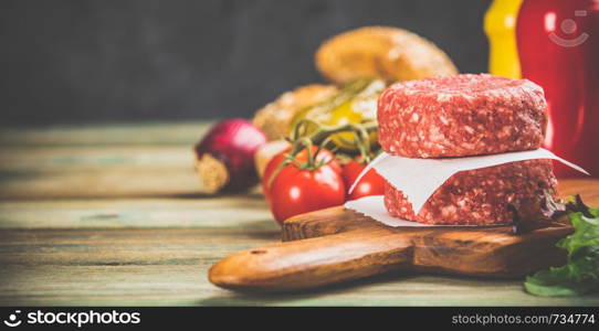 Homemade hamburgers. Raw beef patties and ciabatta bread with other ingredients for hamburgers on wooden background. Homemade hamburgers on wooden table, close up