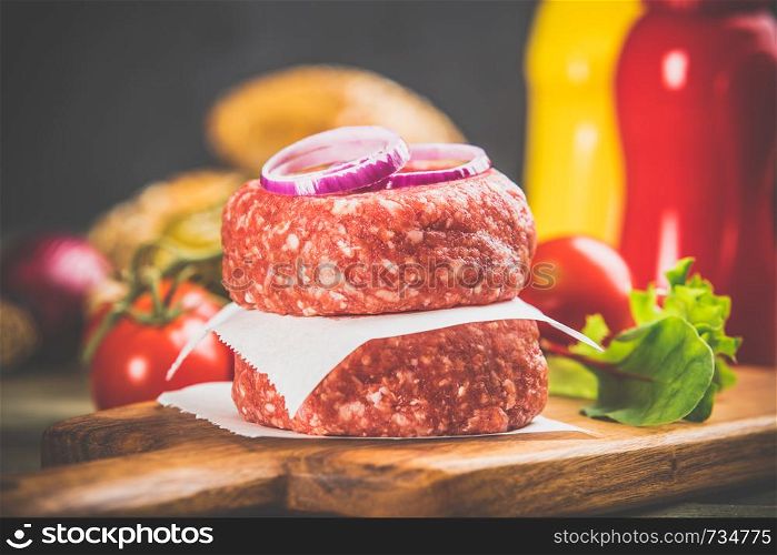 Homemade hamburgers. Raw beef patties and ciabatta bread with other ingredients for hamburgers on wooden background. Homemade hamburgers on wooden table, close up
