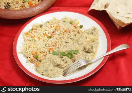 Homemade, indian-style dinner of fish in green curry sauce served with three-coloured vegetable pilau rice and a plate of chappatis.