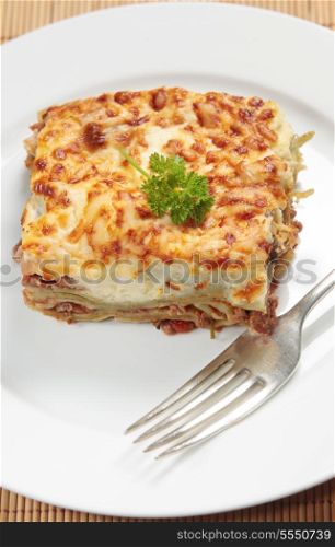 Homemade lasagne verdi on a white plate with a fork, vertical orientation