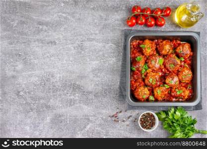 Homemade meatballs with tomato sauce and spices served in black pan on grey background. Tasty cooked meat balls made with minced beef and food ingredients. Top View, Flat lay, banner with copy space. Homemade meatballs with tomato sauce and spices served in black pan on grey concrete background