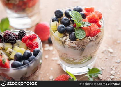 Homemade muesli, bowl of oat granola with yogurt, fresh blueberries, mulberry, strawberries, kiwi, mint and nuts board for healthy breakfast, copy space. Healthy breakfast concept. Clean eating.