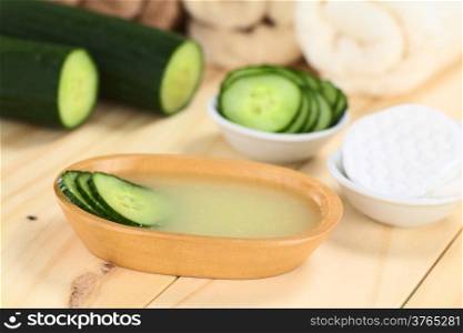 Homemade natural cucumber facial toner that hydrates, softens, soothes and cleanses the skin in a wooden bowl with cucumber slices, with facial pads and towels (Selective Focus, Focus on the front of the cucumber slices in the toner)