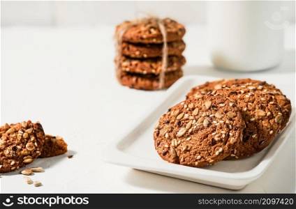 Homemade oatmeal cookies, selective focus. Breakfast idea craft cookies and milk. Handicraft cookies with flax and sesame seeds on a white plate. Festive baked goods