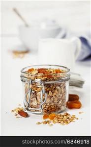 Homemade oatmeal granola with fruits and nuts in a glass jar on white background
