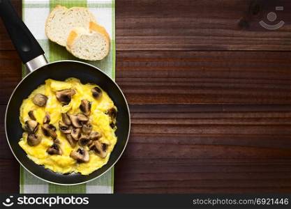 Homemade omelette with mushroom in frying pan with slices of bread on the side, photographed overhead on dark wood with natural light. Omelette with Mushroom