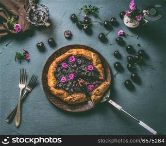 Homemade open cherry pie on wooden plate and rustic kitchen table background with jam and cutlery, top view. Summer berries still life concept