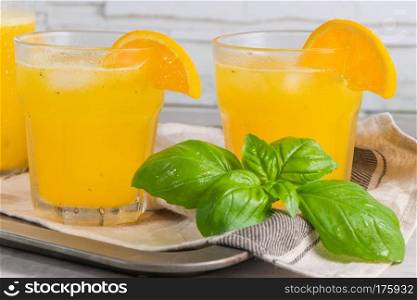 Homemade orange juice with ice cubes and basil leaves in glass on board