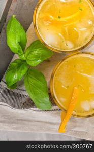 Homemade orange juice with ice cubes and basil leaves in glass on board