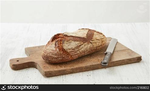 Homemade organic bread on a cutting board with a knife isolated on a white background. Fresh oval organic bread