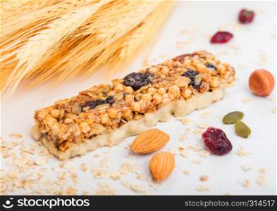 Homemade organic granola cereal bar with nuts and dried fruit on white with oats and raw wheat.