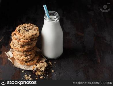 Homemade organic oatmeal cookies with raisins and apricots and bottle of milk on dark wood background.