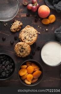 Homemade organic oatmeal cookies with raisins and apricots on wooden background. Black bowl of raisins and dried apricots with flour and fresh fruits.