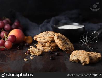 Homemade organic oatmeal cookies with raisins and apricots on wooden background. Black bowl of flour.