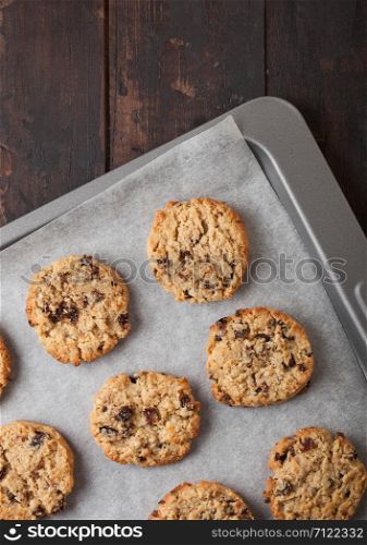 Homemade organic oatmeal cookies with raisins in baking tray on wooden kitchen background.