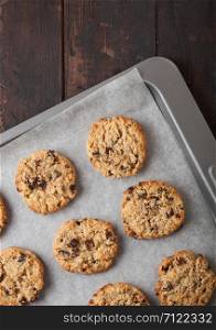 Homemade organic oatmeal cookies with raisins in baking tray on wooden kitchen background.