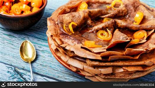 Homemade pancakes with orange candied fruits on a wooden background. Stack of pancakes