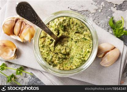 Homemade parsley pesto sauce and ingredients on dark cement background. Close up wiev of basil pesto in glass jar with ingredients.