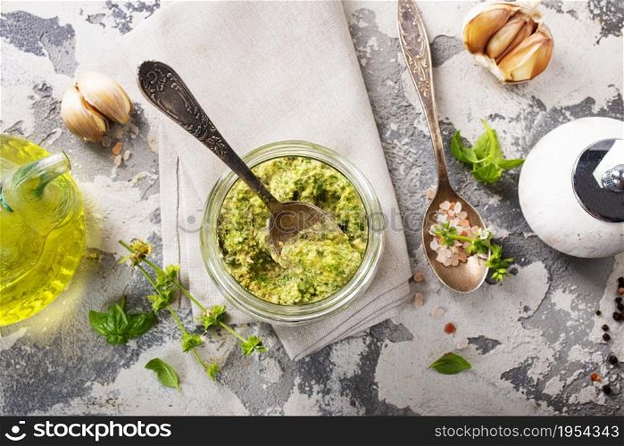 Homemade parsley pesto sauce and ingredients on dark cement background. Close up wiev of basil pesto in glass jar with ingredients.