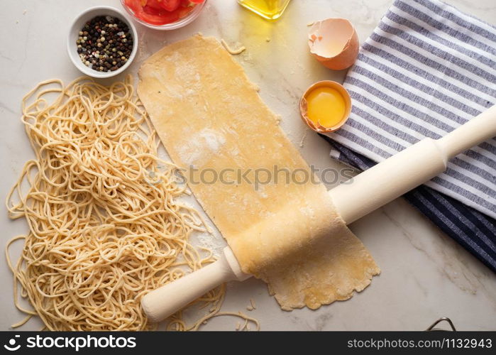 Homemade pasta dough is being processed. Rolled dough for homemade italian uncooked pasta over white marble texture background.