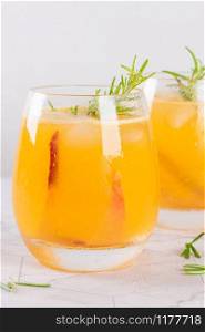 Homemade peach juice with ice cubes and rosemary leaves in glass on marble stone background
