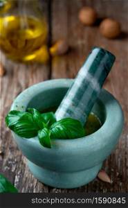 Homemade pesto sauce, prepared in a marble mortar. Ingredients on a wooden table, selective focus on basil leaves on a mortar, close-up