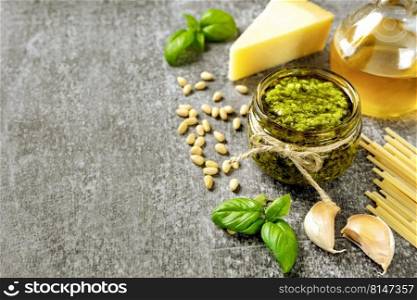 Homemade pesto sauce with ingredients. Sauce pesto in white bowl with basil, olive oil, pine nuts and parmesan cheese on gray concrete background with copy space for text.. Homemade pesto sauce with food ingredients on gray background