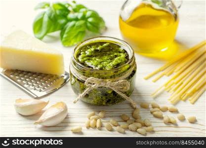 Homemade pesto sauce with ingredients. Sauce pesto in white bowl with basil, olive oil, pine nuts, pasta and parmesan cheese on white wooden background. Homemade pesto sauce with food ingredients on white wooden background