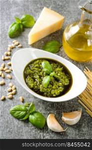 Homemade pesto sauce with ingredients. Sauce pesto in white bowl with basil, olive oil, pine nuts and parmesan cheese on gray concrete background. Homemade pesto sauce with food ingredients on gray background