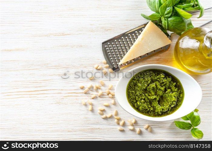 Homemade pesto sause with ingredients. Sause pesto in white bowl with basil, olive oil, pine nuts and parmesan cheese on white wooden background. Top view, flat lay with copy space for text.. Homemade pesto sause with food ingredients on white wooden background
