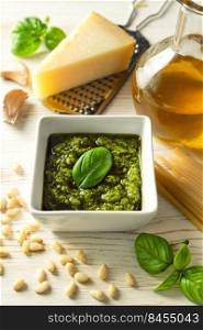 Homemade pesto sause with ingredients. Sause pesto in white bowl with basil, olive oil, pine nuts and parmesan cheese on white wooden background with copy space for text.. Homemade pesto sause with food ingredients on white wooden background