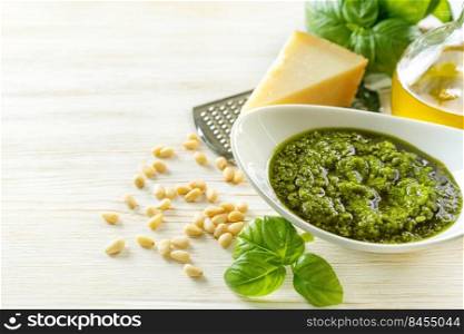 Homemade pesto sause with ingredients. Sause pesto in white bowl with basil, olive oil, pine nuts and parmesan cheese on white wooden background with copy space for text.. Homemade pesto sause with food ingredients on white wooden background
